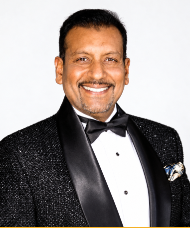 Christopher “Chris” Nazir smiling in a tuxedo against a white background