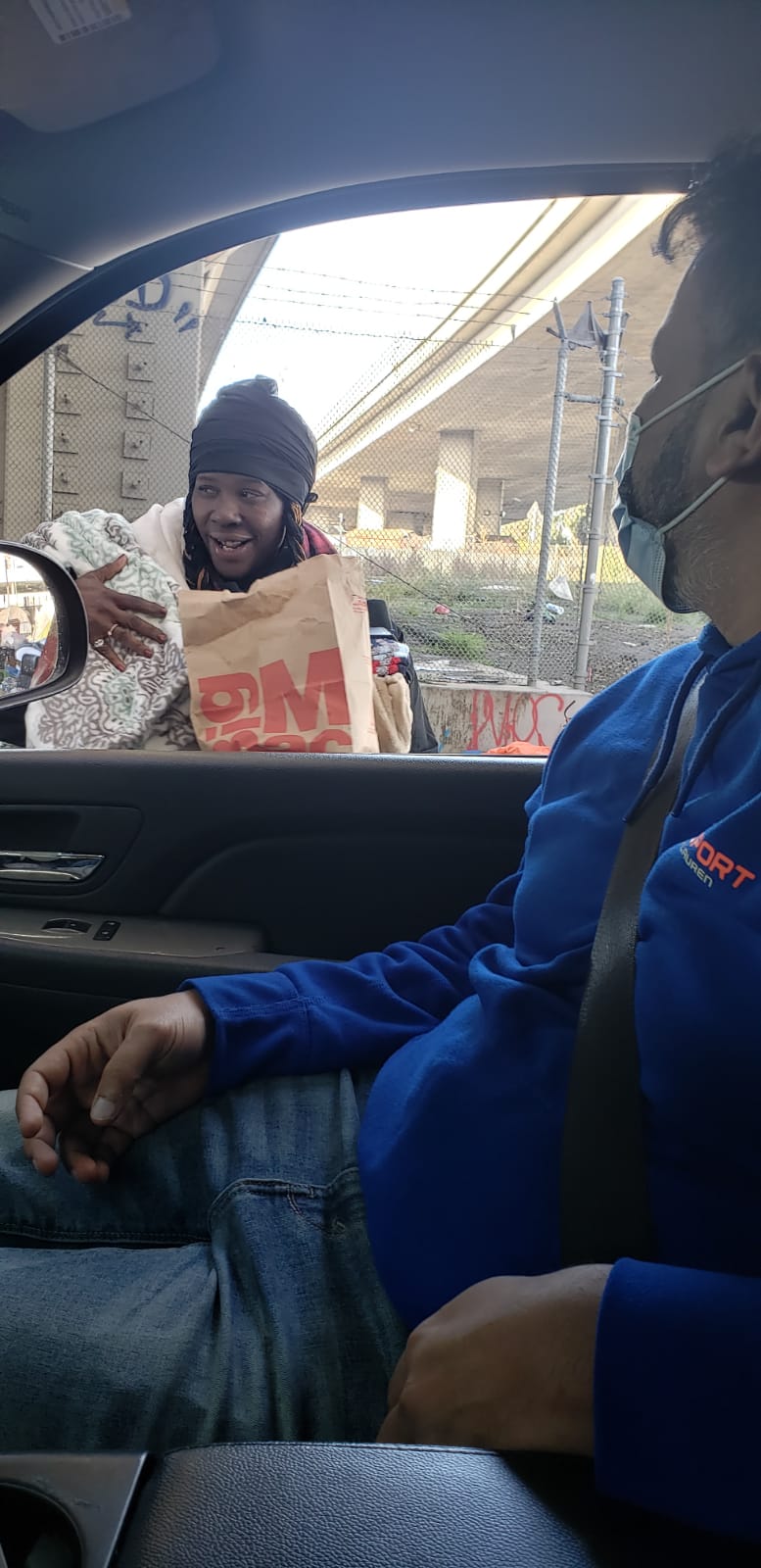 A person receiving a bag of supplies through a car window